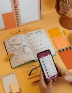 mãos mexendo em celular ao lado de caderno