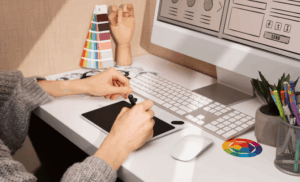 mãos mexendo em computador com ítens de design ao redor